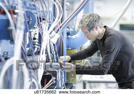 Stock Image - Mid adult male technician maintaining cables in engineering plant. Fotosearch