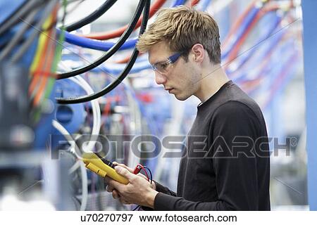 Stock Photo - Mid adult male technician testing cables in engineering plant. Fotosearch