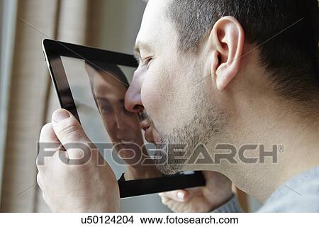 Picture - Mid adult man kissing screen of digital tablet. Fotosearch