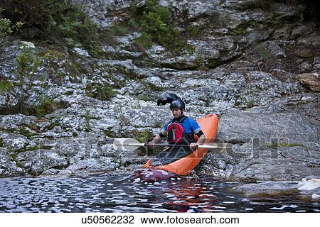 Stock Image - Mid adult man moving kayak from waters edge into river. Fotosearch