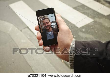 Picture - Mid adult man on sidewalk holding smartphone with photograph on screen. Fotosearch