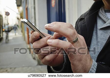 Stock Photo - Mid adult man on sidewalk using touchscreen on smartphone. Fotosearch