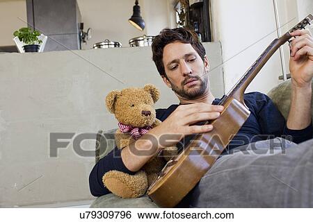 Mid adult man reclining on sofa playing guitar View Large Photo Image Stock Photograph - Mid adult man reclining on sofa playing guitar. Fotosearch