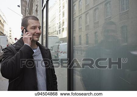 Stock Photo - Mid adult man talking on smartphone while window shopping. Fotosearch