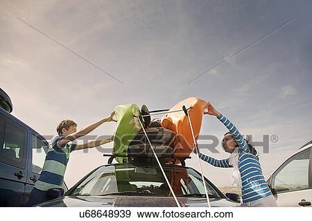 Stock Photo - Mother and son stacking kayaks on top of car. Fotosearch