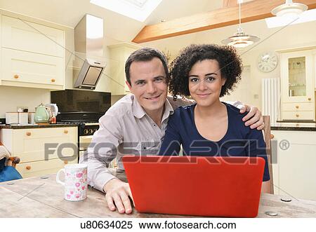 Stock Photography - Portrait of couple with laptop on kitchen table. Fotosearch