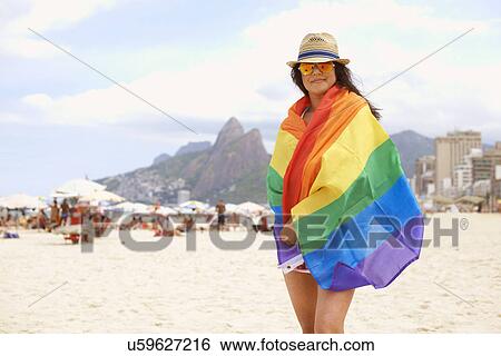 Stock Photograph - Portrait of mature woman wrapped in multicolored flag, Ipanema beach, Rio De Janeiro, Brazil. Fotosearch