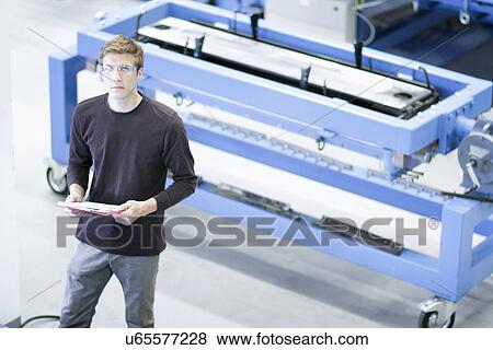 Stock Photo - Portrait of mid adult male with paperwork in engineering plant. Fotosearch