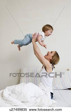 Stock Photography - Portrait of mid adult woman holding up her one year old baby girl. Fotosearch