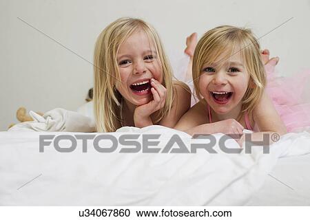 Stock Image - Portrait of two young sisters lying on front in bed. Fotosearch