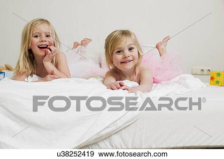 Portrait of two young sisters lying on bed View Large Photo Image Stock Photo - Portrait of two young sisters lying on bed. Fotosearch
