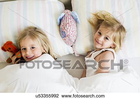 Portrait of two young sisters lying side by side in bed View Large Photo Image Stock Image - Portrait of two young sisters lying side by side in bed. Fotosearch