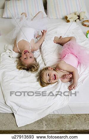 Stock Image - Portrait of two young sisters playing on bed. Fotosearch