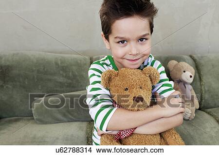 Picture - Portrait of young boy on sofa hugging teddy. Fotosearch