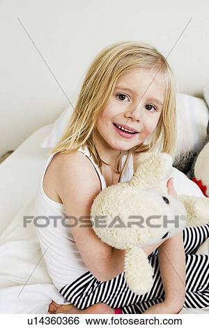 Portrait of young girl kneeling on bed with soft toy View Large Photo Image Stock Photograph - Portrait of young girl kneeling on bed with soft toy. Fotosearch
