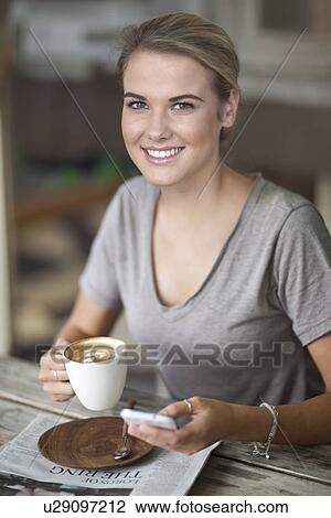 Portrait of young woman sitting in cafe with coffee cup and cellphone View Large Photo Image Stock Image - Portrait of young woman sitting in cafe with coffee cup and cellphone. Fotosearch