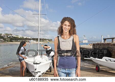Stock Photography - Portrait of young woman with friends preparing sailboat. Fotosearch