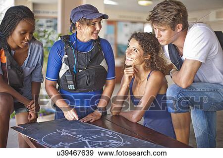 Stock Photo - Sailing friends looking at blackboard diagram on table. Fotosearch