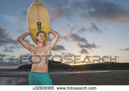 Surfer standing on beach carrying surfboard View Large Photo Image Stock Photography - Surfer standing on beach carrying surfboard. Fotosearch