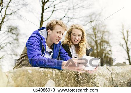 Stock Image - Teenage brother and sister looking at digital tablet on rural bridge. Fotosearch