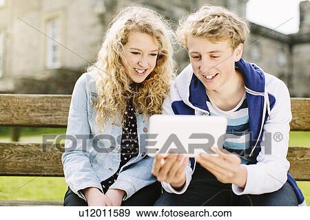 Teenage brother and sister looking at digital tablet on bench View Large Photo Image Stock Photo - Teenage brother and sister looking at digital tablet on bench. Fotosearch