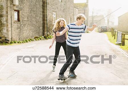 Teenage brother and sister skateboarding on rural road View Large Photo Image Picture - Teenage brother and sister skateboarding on rural road. Fotosearch