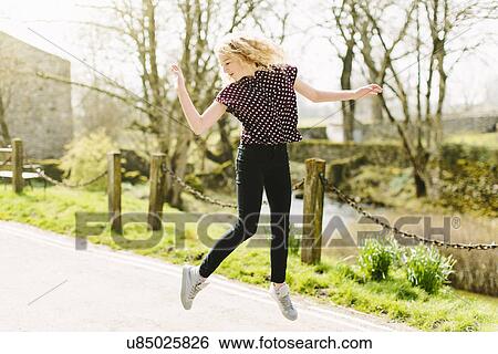 Stock Photograph - Teenage girl jumping mid air on rural road. Fotosearch