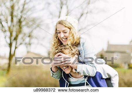 Teenage girl on piggyback covering teenage boys eyes View Large Photo Image Stock Image - Teenage girl on piggyback covering teenage boys eyes. Fotosearch
