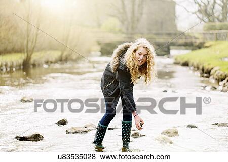 Stock Photo - Teenage girl picking up stones in rural river. Fotosearch