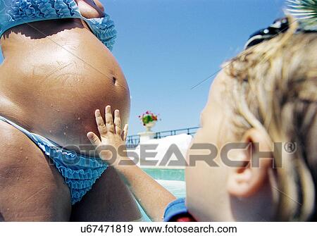 Stock Photo - Toddler touching mother's pregnant bump. Fotosearch