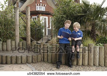 Picture - Two school boys reading book on log fence. Fotosearch