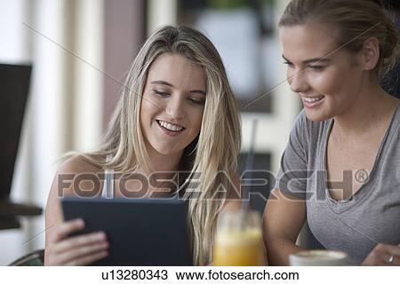Two young adult female friends looking at digital tablet in cafe View Large Photo Image Stock Image - Two young adult female friends looking at digital tablet in cafe. Fotosearch