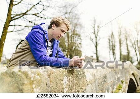 Picture - Unhappy teenage boy leaning over rural bridge. Fotosearch