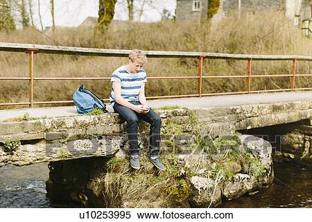 Unhappy teenage boy looking down from rural bridge View Large Photo Image Stock Photography - Unhappy teenage boy looking down from rural bridge. Fotosearch