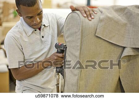 Stock Photo - Upholsterer attaching textile to sofa using staple gun. Fotosearch