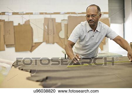 Stock Image - Upholsterer measuring leather on workbench. Fotosearch