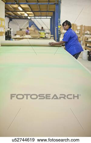 Stock Photo - Upholsterer unrolling a length of textile on workbench. Fotosearch
