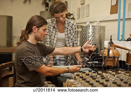 Picture - Woman and man looking at bottle in distillery. Fotosearch