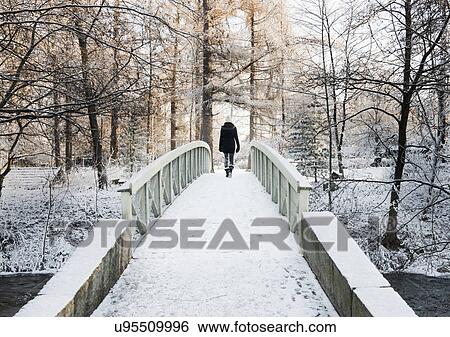 Stock Photograph - Woman crossing snow-covered bridge, rear view. Fotosearch