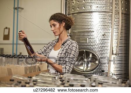 Stock Image - Woman looking at bottle in distillery. Fotosearch