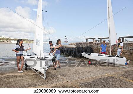 Young adult friends preparing sailboats on waterfront View Large Photo Image Stock Photo - Young adult friends preparing sailboats on waterfront. Fotosearch
