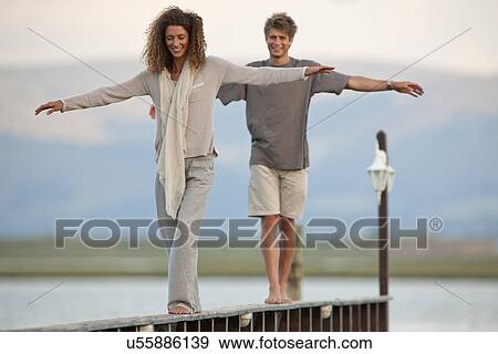 Young couple balancing on jetty View Large Photo Image Stock Photo - Young couple balancing on jetty. Fotosearch