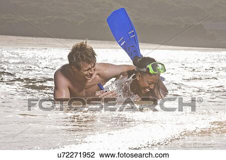 Stock Image - Young couple lying in sea, wearing snorkel. Fotosearch