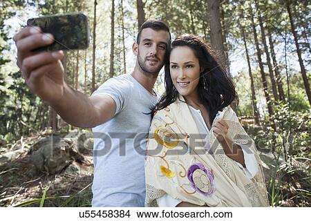 Picture - Young couple taking self portrait photograph in forest. Fotosearch