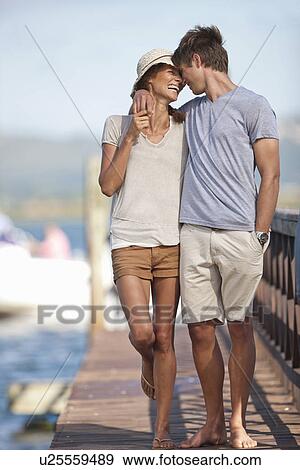 Stock Photo - Young couple walking along jetty, arms around each other. Fotosearch