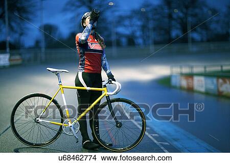 Picture - Young female cyclist drinking from water bottle at velodrome track. Fotosearch