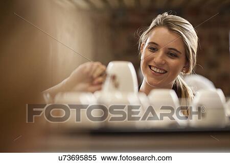 Stock Photography - Young female waitress picking up cup from tray in cafe. Fotosearch