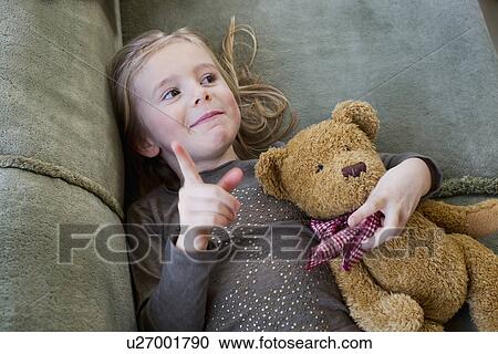 Stock Image - Young girl lying on sofa with her teddy bear. Fotosearch