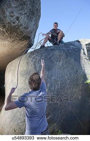 Stock Image - Young male climbers reaching out for each other on rock. Fotosearch