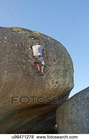 Stock Photo - Young man climbing with ropes on boulder. Fotosearch